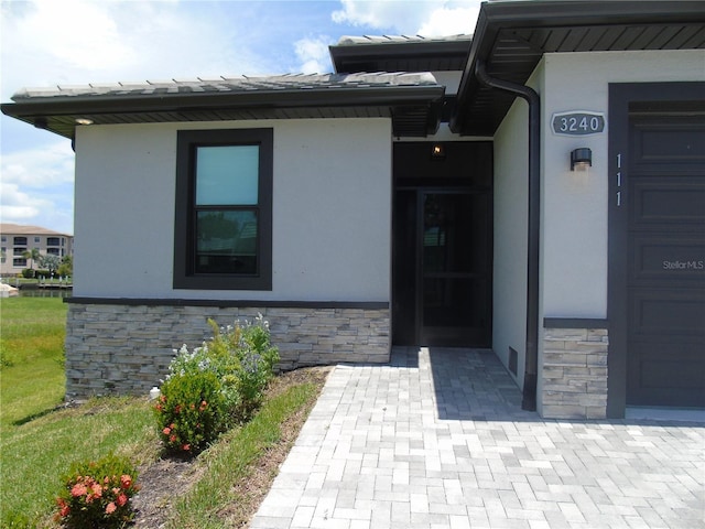 view of exterior entry with visible vents, stone siding, and stucco siding