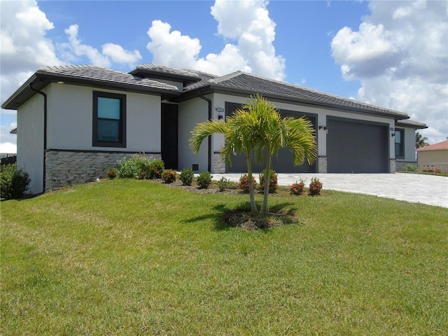 prairie-style home with a front yard, an attached garage, stucco siding, stone siding, and decorative driveway