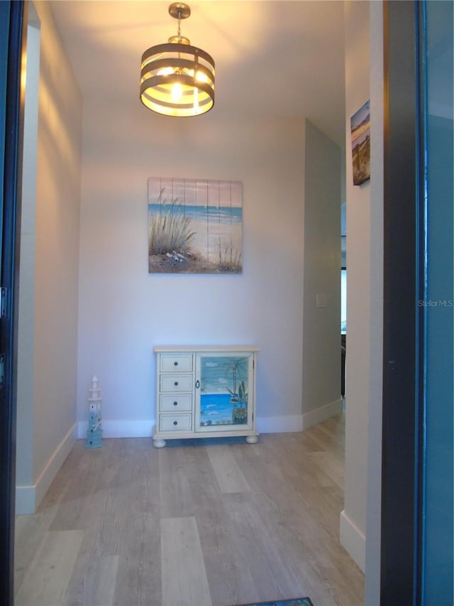 hall featuring a chandelier, baseboards, and wood finished floors