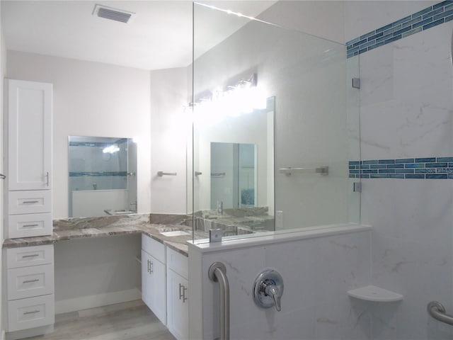 full bathroom featuring vanity, a shower with shower door, wood finished floors, and visible vents