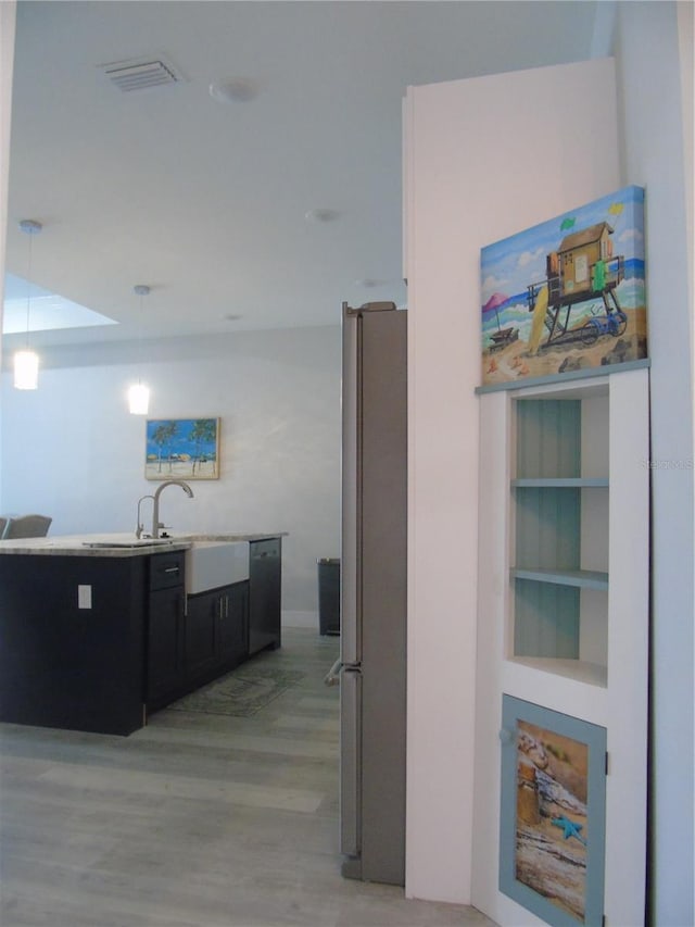 interior space with light wood finished floors, black dishwasher, freestanding refrigerator, hanging light fixtures, and dark cabinets