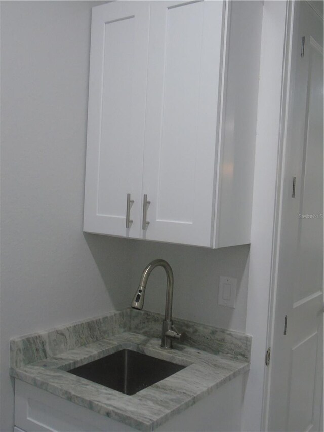 kitchen featuring white cabinets, light stone countertops, and sink