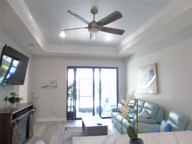 living room with ceiling fan, light hardwood / wood-style floors, ornamental molding, and a tray ceiling