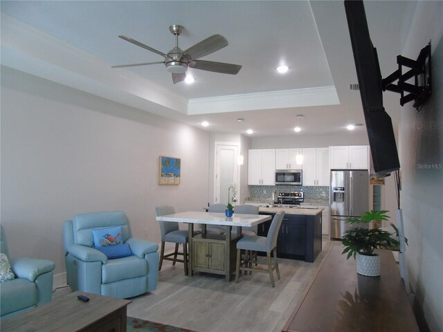 living room featuring light wood finished floors, a tray ceiling, recessed lighting, ornamental molding, and ceiling fan