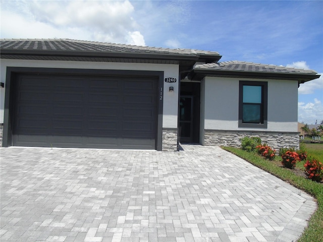 prairie-style house with a tiled roof, stucco siding, a garage, stone siding, and driveway