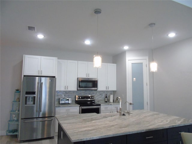 kitchen with visible vents, a center island with sink, stainless steel appliances, white cabinetry, and backsplash