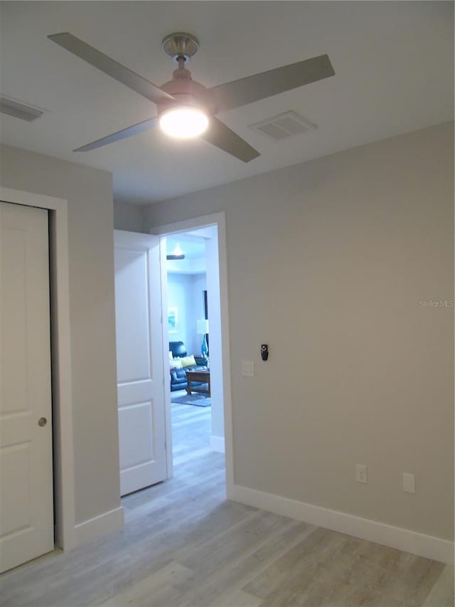 empty room with a ceiling fan, visible vents, light wood finished floors, and baseboards