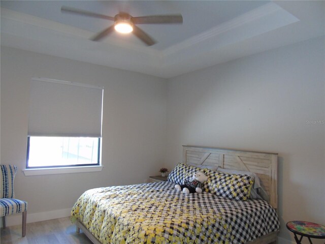 bedroom featuring ceiling fan, baseboards, a tray ceiling, and wood finished floors