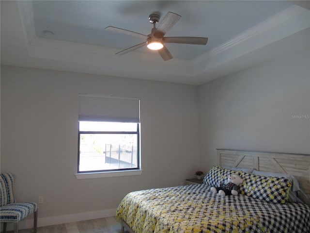 bedroom featuring ceiling fan, baseboards, a tray ceiling, and wood finished floors