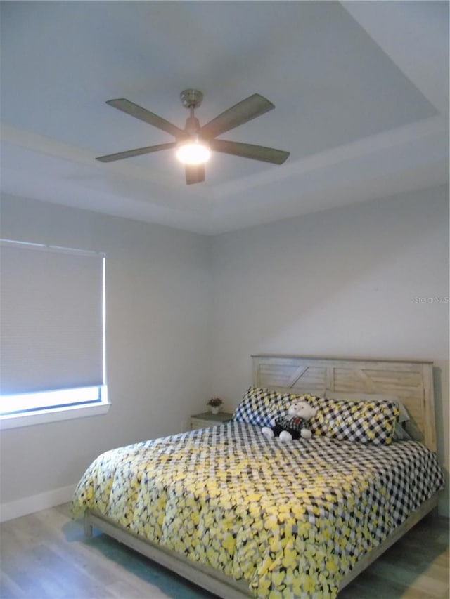 bedroom featuring ceiling fan, a tray ceiling, baseboards, and wood finished floors