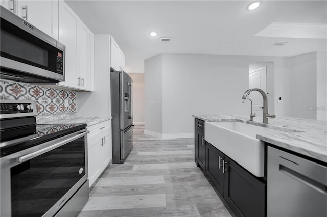kitchen with light stone counters, a sink, white cabinetry, stainless steel appliances, and decorative backsplash