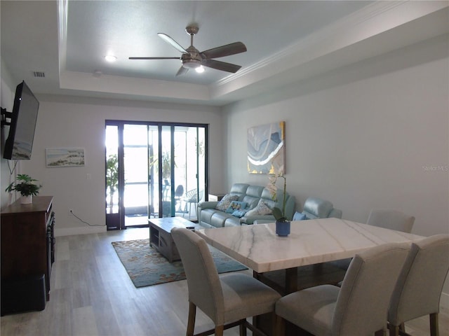 dining space with visible vents, baseboards, ceiling fan, light wood-type flooring, and a tray ceiling