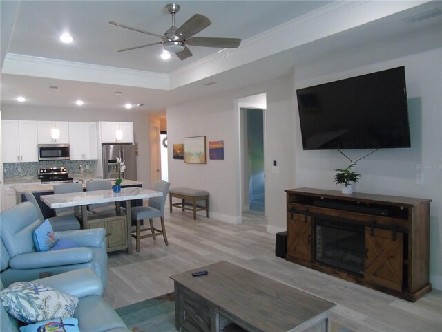 living room featuring a raised ceiling, ornamental molding, light wood-type flooring, ceiling fan, and recessed lighting