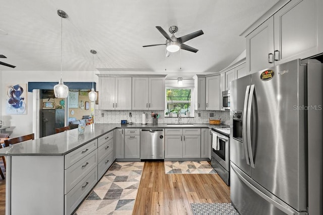 kitchen with light wood-type flooring, kitchen peninsula, gray cabinets, stainless steel appliances, and decorative backsplash