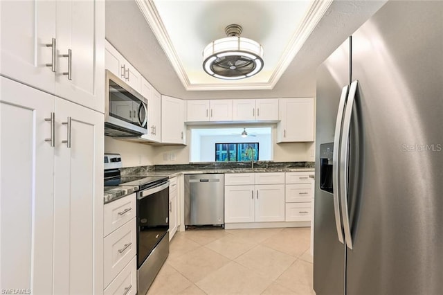 kitchen with stainless steel appliances, a tray ceiling, white cabinets, and light tile floors