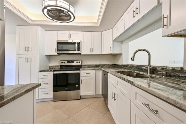 kitchen with dark stone counters, a tray ceiling, stainless steel appliances, sink, and white cabinetry