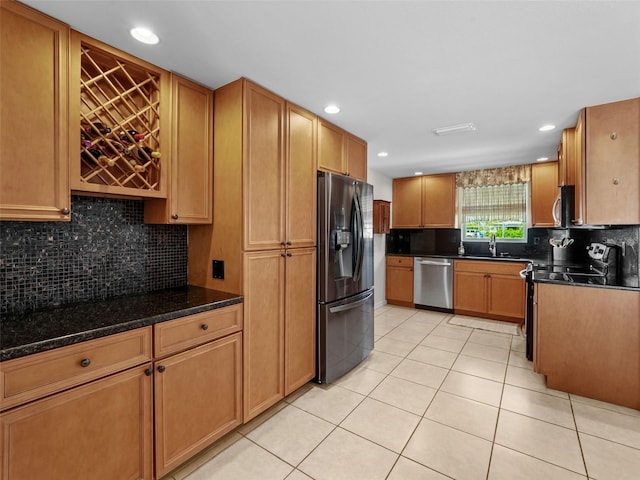 kitchen with sink, light tile patterned floors, dark stone countertops, appliances with stainless steel finishes, and backsplash