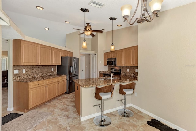 kitchen with decorative backsplash, appliances with stainless steel finishes, pendant lighting, and dark stone counters