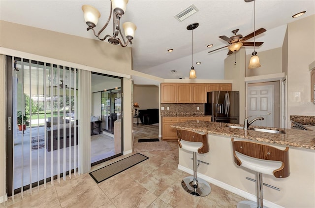 kitchen with tasteful backsplash, stone counters, ceiling fan with notable chandelier, stainless steel fridge with ice dispenser, and sink