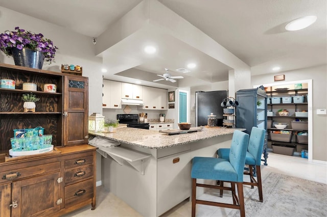 kitchen featuring a breakfast bar area, stainless steel refrigerator, white cabinetry, black range with electric cooktop, and kitchen peninsula