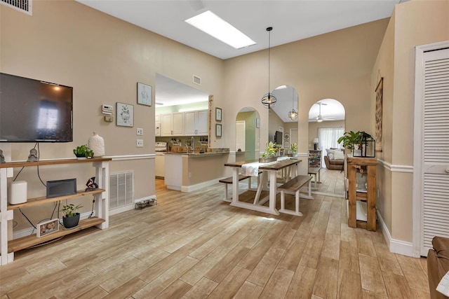 dining space with ceiling fan, light hardwood / wood-style floors, and a towering ceiling