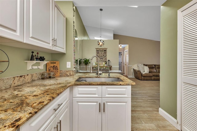 kitchen featuring white cabinets, sink, vaulted ceiling, light stone countertops, and decorative light fixtures