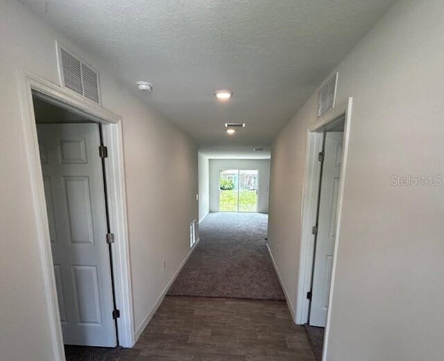 hall with dark colored carpet and a textured ceiling