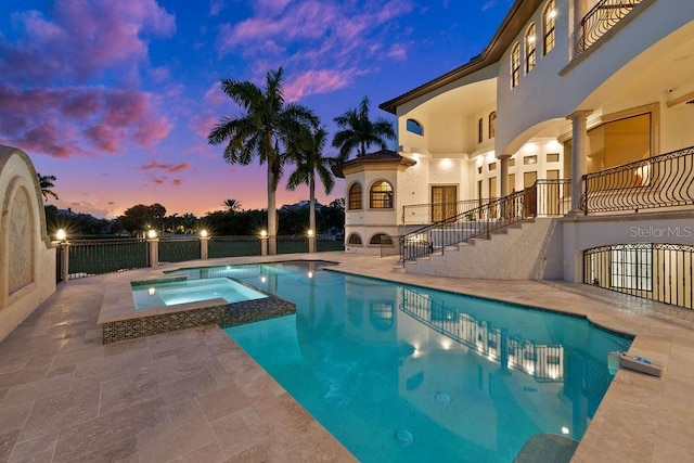 pool at dusk with an in ground hot tub and a patio area