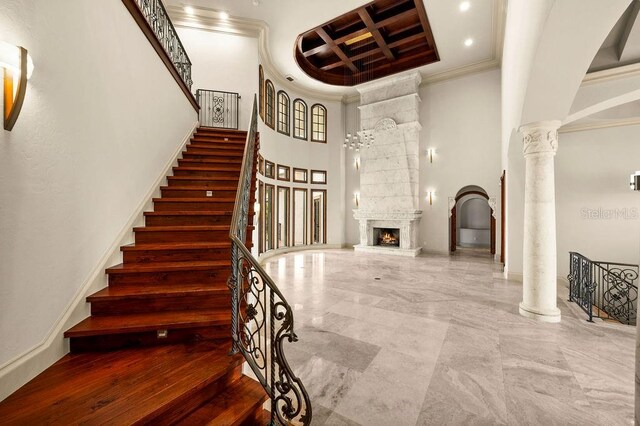 interior space featuring a fireplace, ornamental molding, coffered ceiling, ornate columns, and a towering ceiling