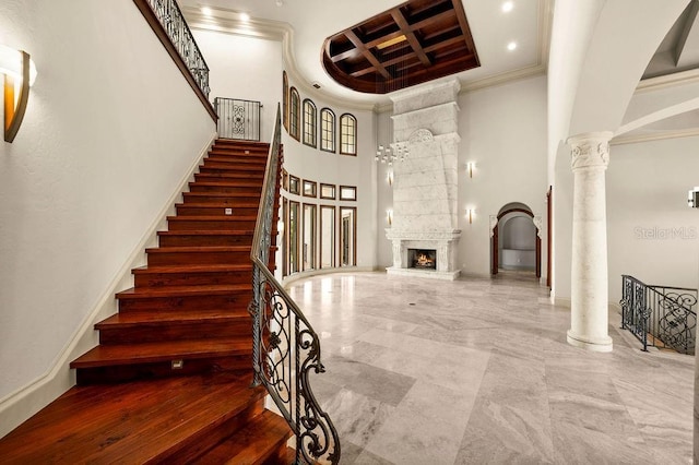 stairway with ornamental molding, coffered ceiling, a large fireplace, decorative columns, and a towering ceiling