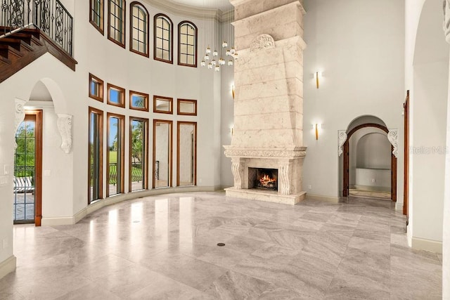 unfurnished living room featuring a premium fireplace, arched walkways, baseboards, and a towering ceiling