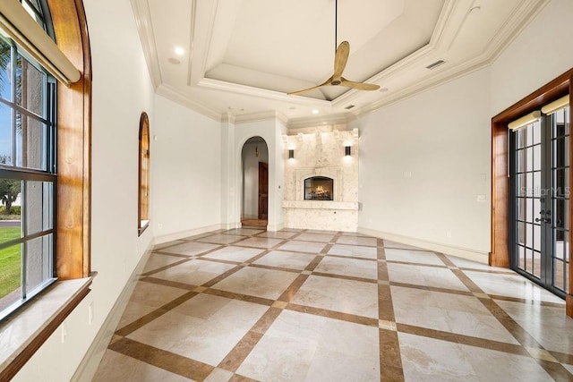 unfurnished living room featuring a warm lit fireplace, crown molding, a raised ceiling, and baseboards