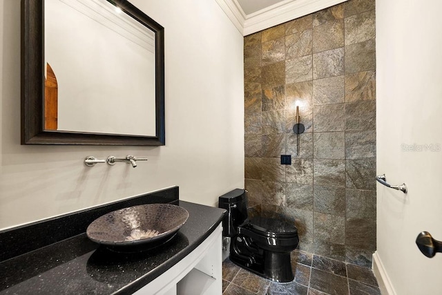 bathroom with toilet, ornamental molding, a tile shower, stone finish floor, and vanity