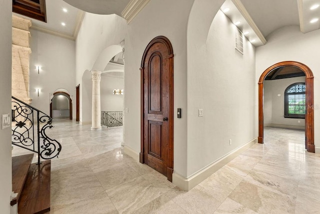 hallway with a high ceiling, decorative columns, light tile patterned floors, and crown molding