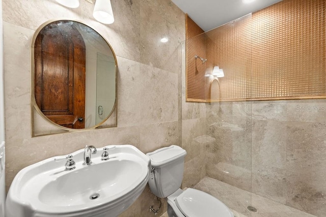 bathroom with sink, toilet, a tile shower, and tile walls