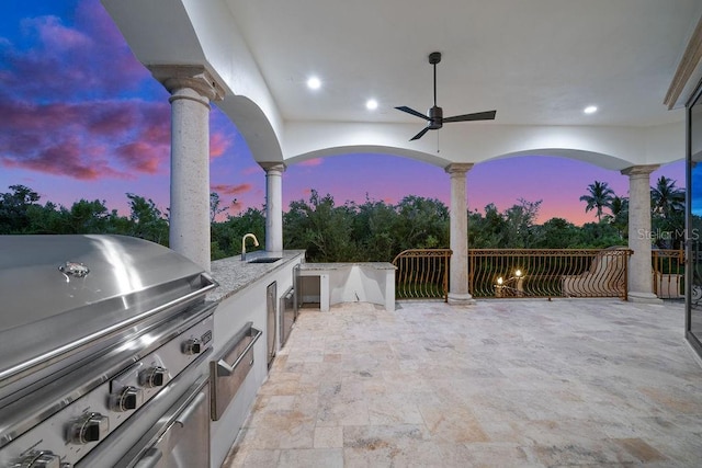 patio terrace at dusk featuring exterior kitchen, sink, ceiling fan, and grilling area