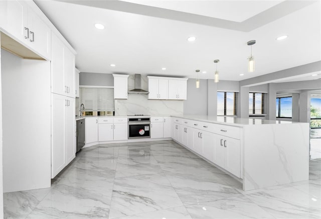 kitchen with wall chimney range hood, hanging light fixtures, appliances with stainless steel finishes, white cabinetry, and kitchen peninsula