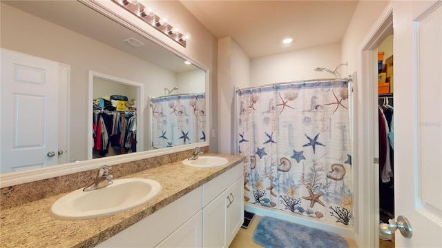 full bathroom with double vanity, a spacious closet, and a sink