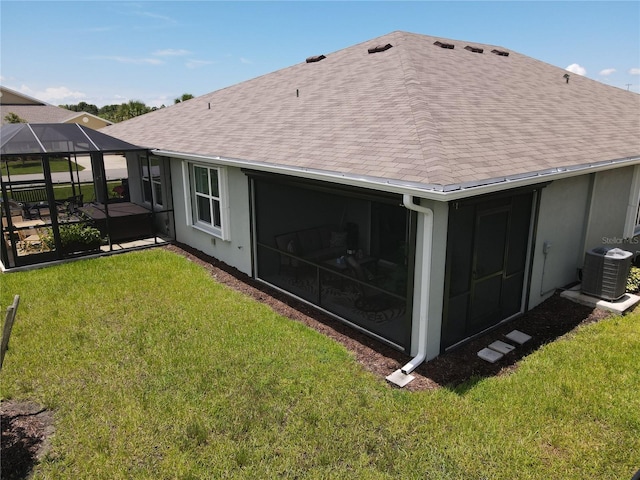 rear view of house with a yard, roof with shingles, cooling unit, and glass enclosure