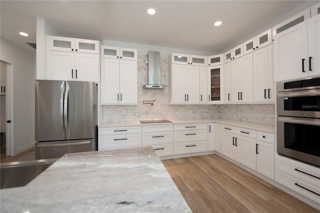 kitchen featuring tasteful backsplash, appliances with stainless steel finishes, white cabinets, wall chimney exhaust hood, and light stone counters