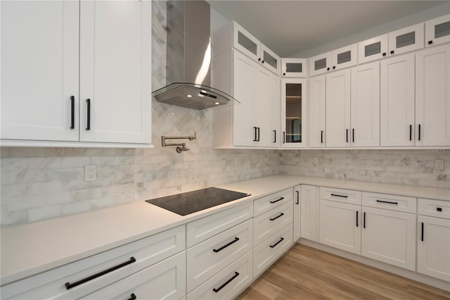 kitchen with backsplash, wall chimney range hood, black electric stovetop, light hardwood / wood-style floors, and white cabinets