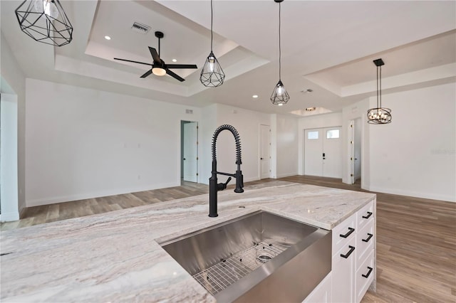 kitchen featuring a raised ceiling, light stone countertops, hanging light fixtures, and white cabinetry