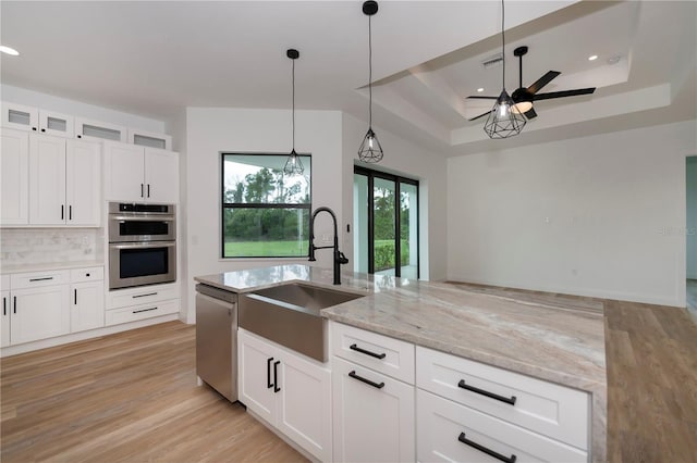 kitchen featuring white cabinets, light stone counters, sink, and a tray ceiling