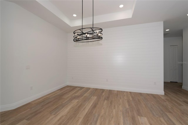 empty room with light wood-type flooring, a notable chandelier, and a tray ceiling