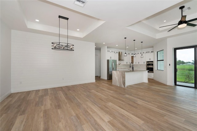 kitchen with pendant lighting, white cabinets, a center island with sink, and a tray ceiling