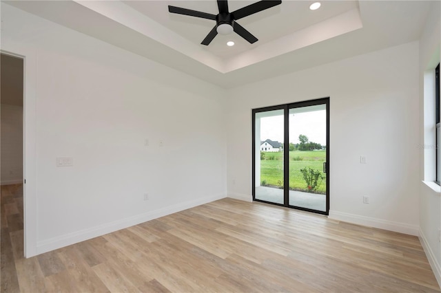 spare room with ceiling fan, light wood-type flooring, and a tray ceiling