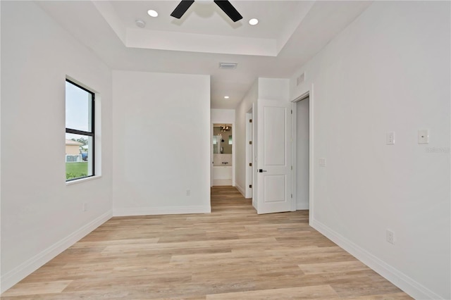 empty room with light wood-type flooring, ceiling fan, and a raised ceiling