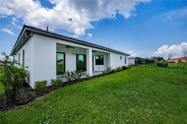 rear view of property featuring ceiling fan, a patio area, and a lawn