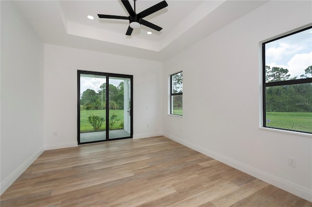 empty room featuring ceiling fan, light hardwood / wood-style floors, and a raised ceiling