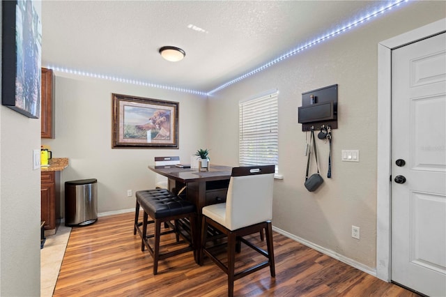 dining room featuring light wood-type flooring, a textured ceiling, and baseboards
